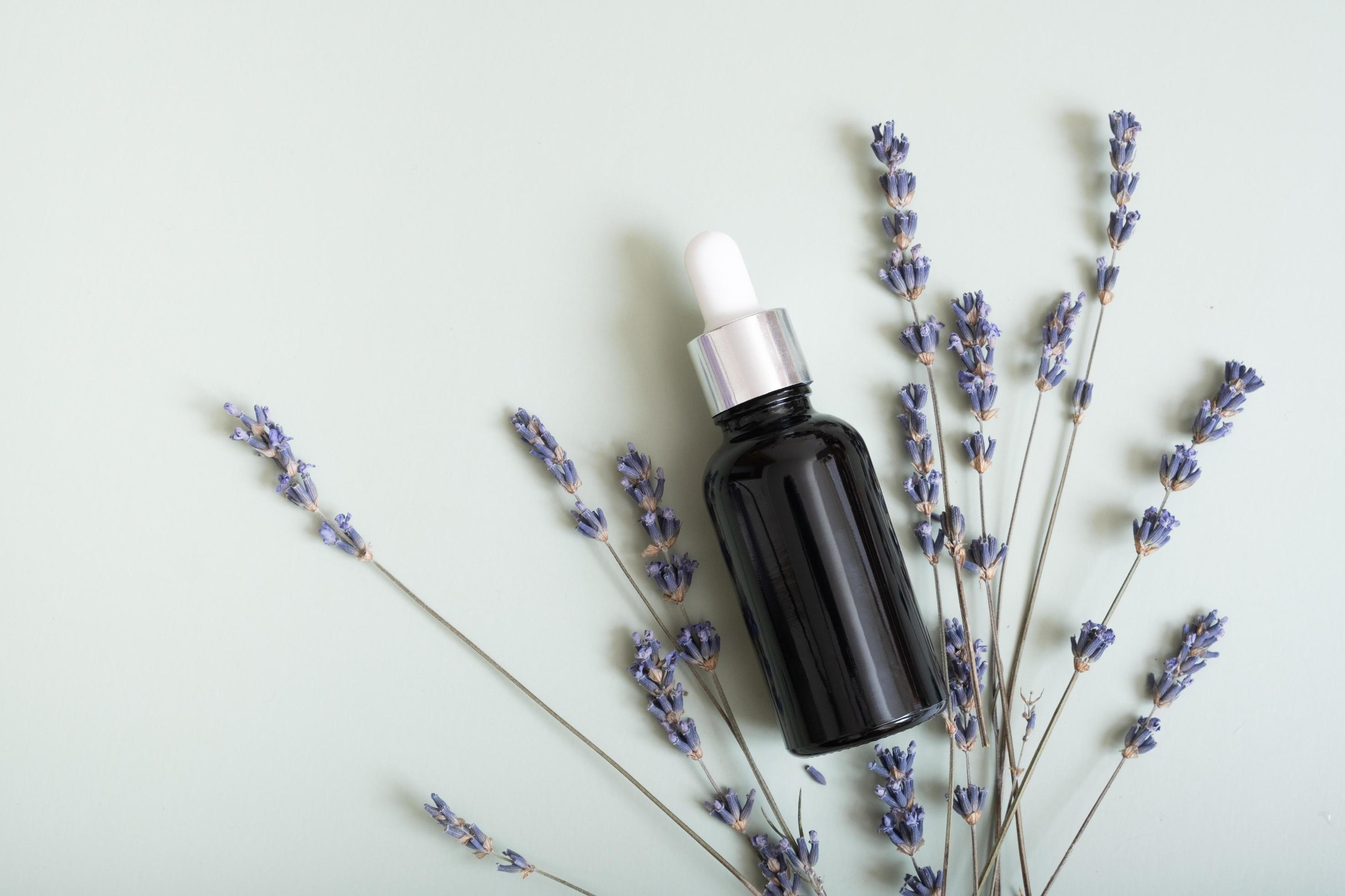 Cosmetic bottle with pipette on wooden slice top view, flat lay on colored background with lavender flowers. Natural cosmetic concept Stock Free