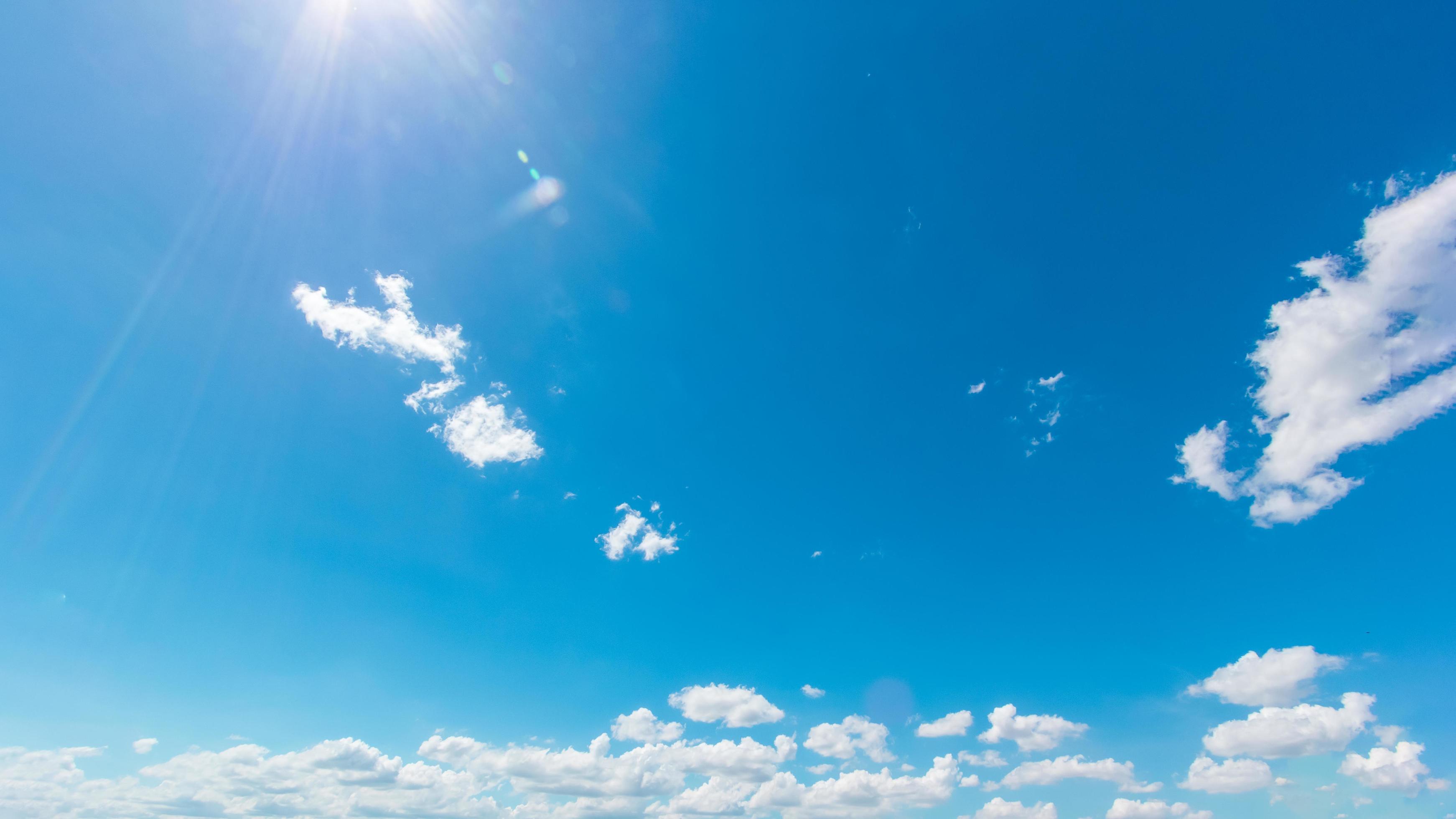 Natural abstract background of bright blue sky and fluffy white clouds on a sunny, light a flare and sun. Stock Free