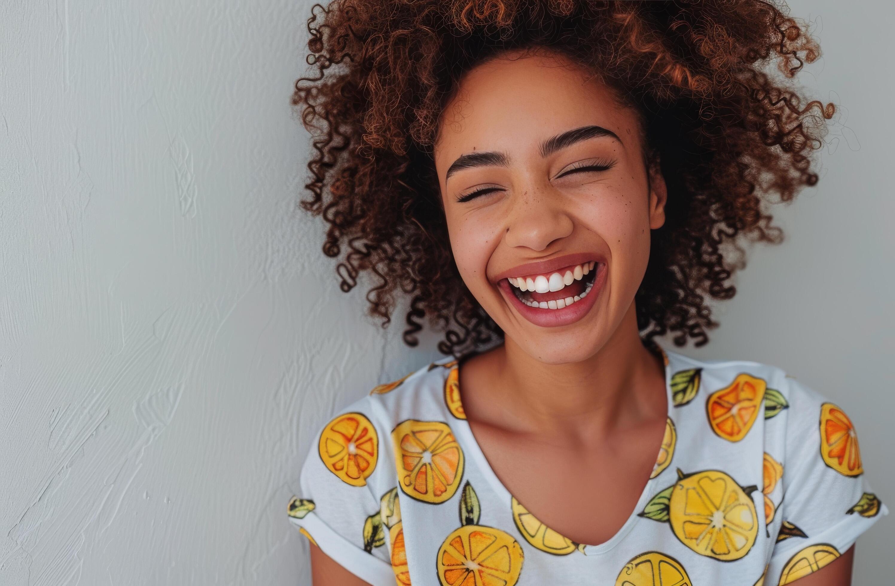 Woman With Curly Hair Smiles Against a Green Wall While Wearing a Lemon-Patterned Shirt Stock Free