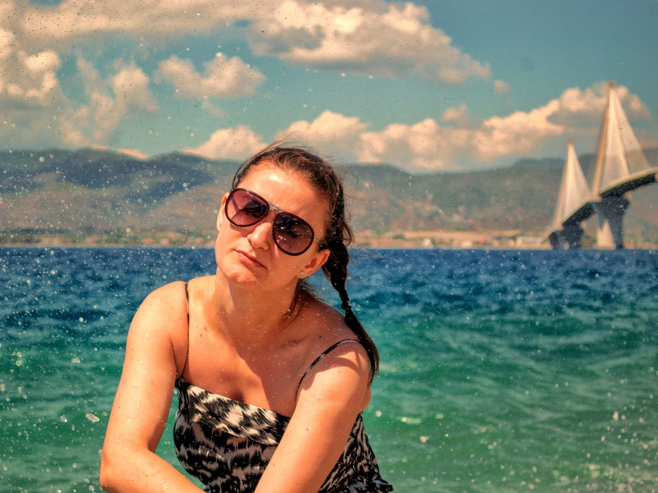 Beautiful Woman Wearing Glasses being Splashed by The Sea with Greek Rio-Antirio Bridge in the Background Stock Free