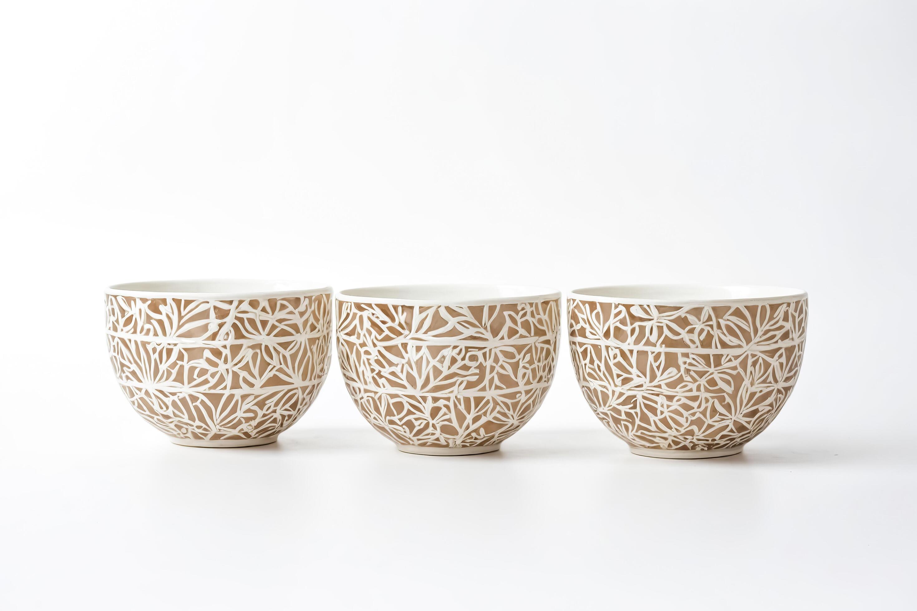 Three Ceramic Bowls with Intricate White Floral Design on Brown Background Stock Free