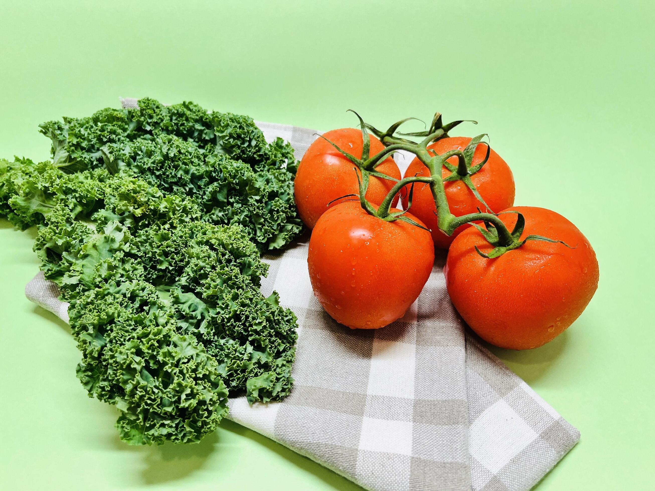 Kale leaf salad and tomato vegetable on green background. Creative layout made of kale and tomato closeup. Food concept. Stock Free