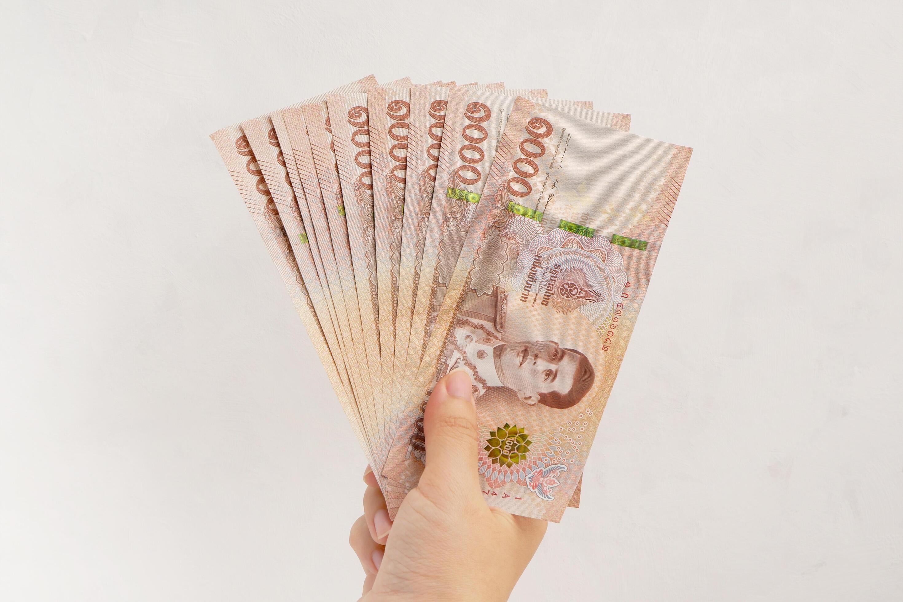 Hand holding new 1000 Thai Baht banknotes on white wall background. Business and finance concept. Stock Free