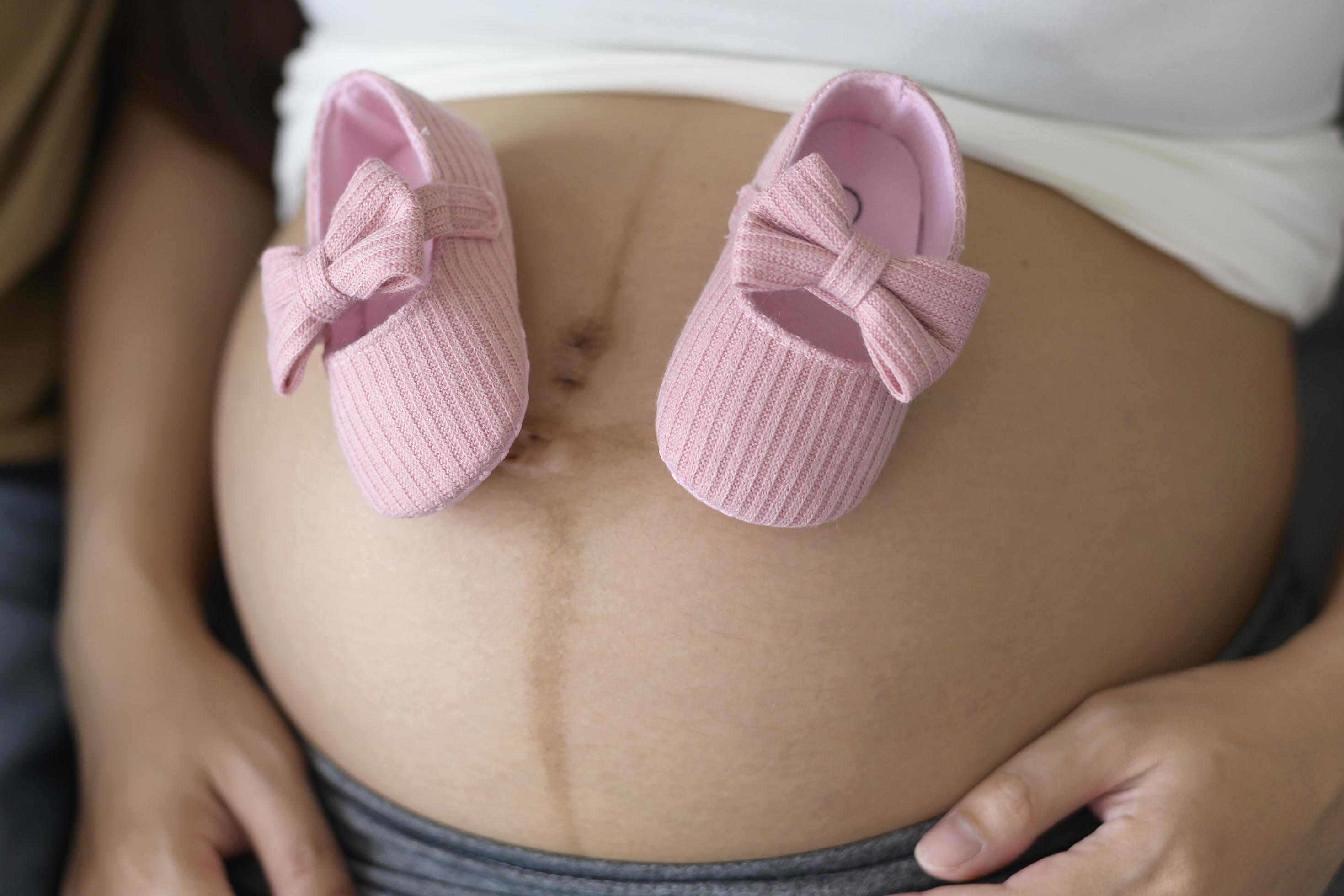 Young pregnant woman putting baby shoes on tummy, family and pregnancy care concept Stock Free