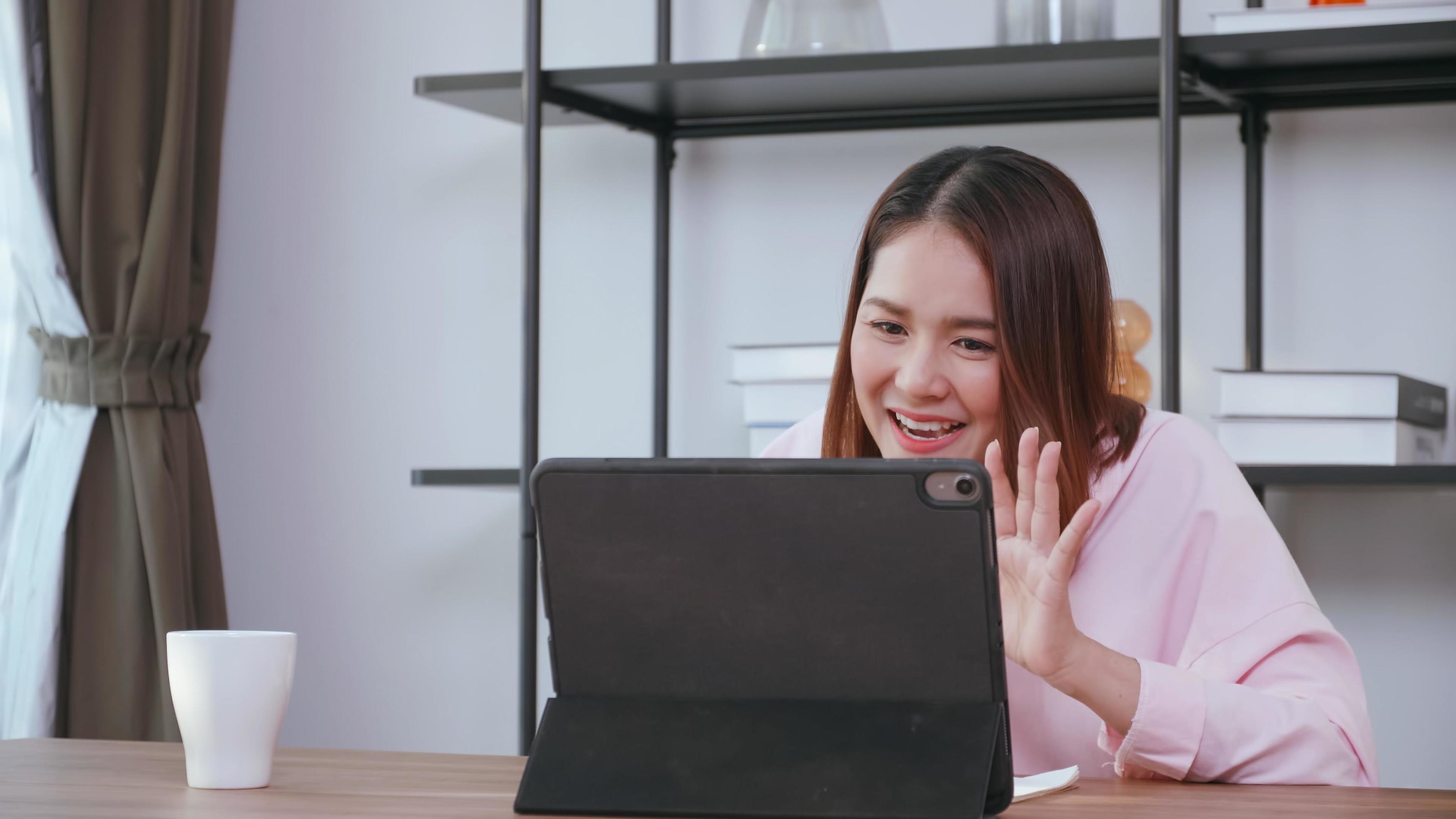 A young woman having video call with family on tablet computer at home. Stock Free