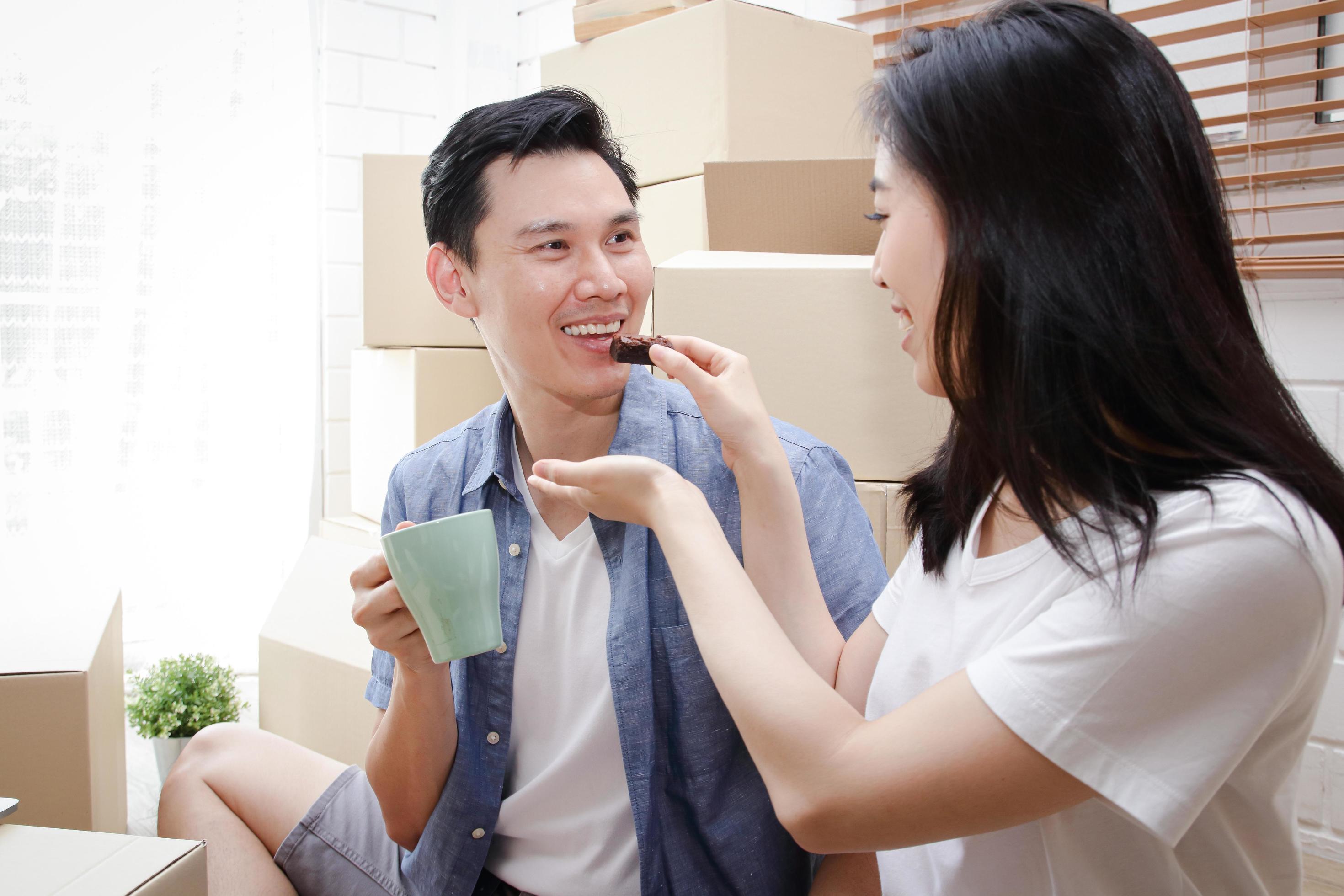 Happy smiling Asian couple moving into a new home The wife feeds her husband snacks. Family concept, the beginning of a new life. Stock Free