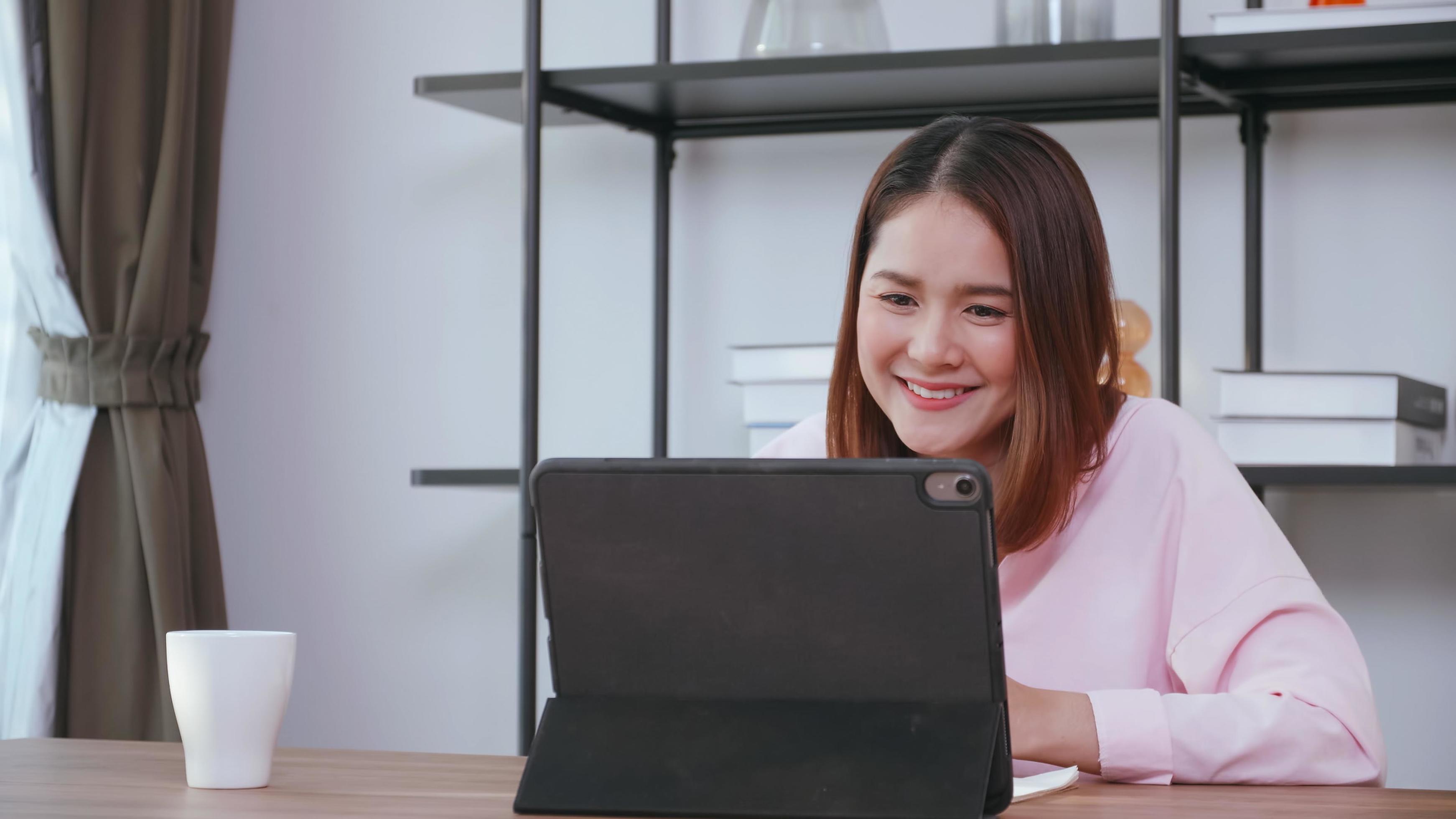 A young woman having video call with family on tablet computer at home. Stock Free