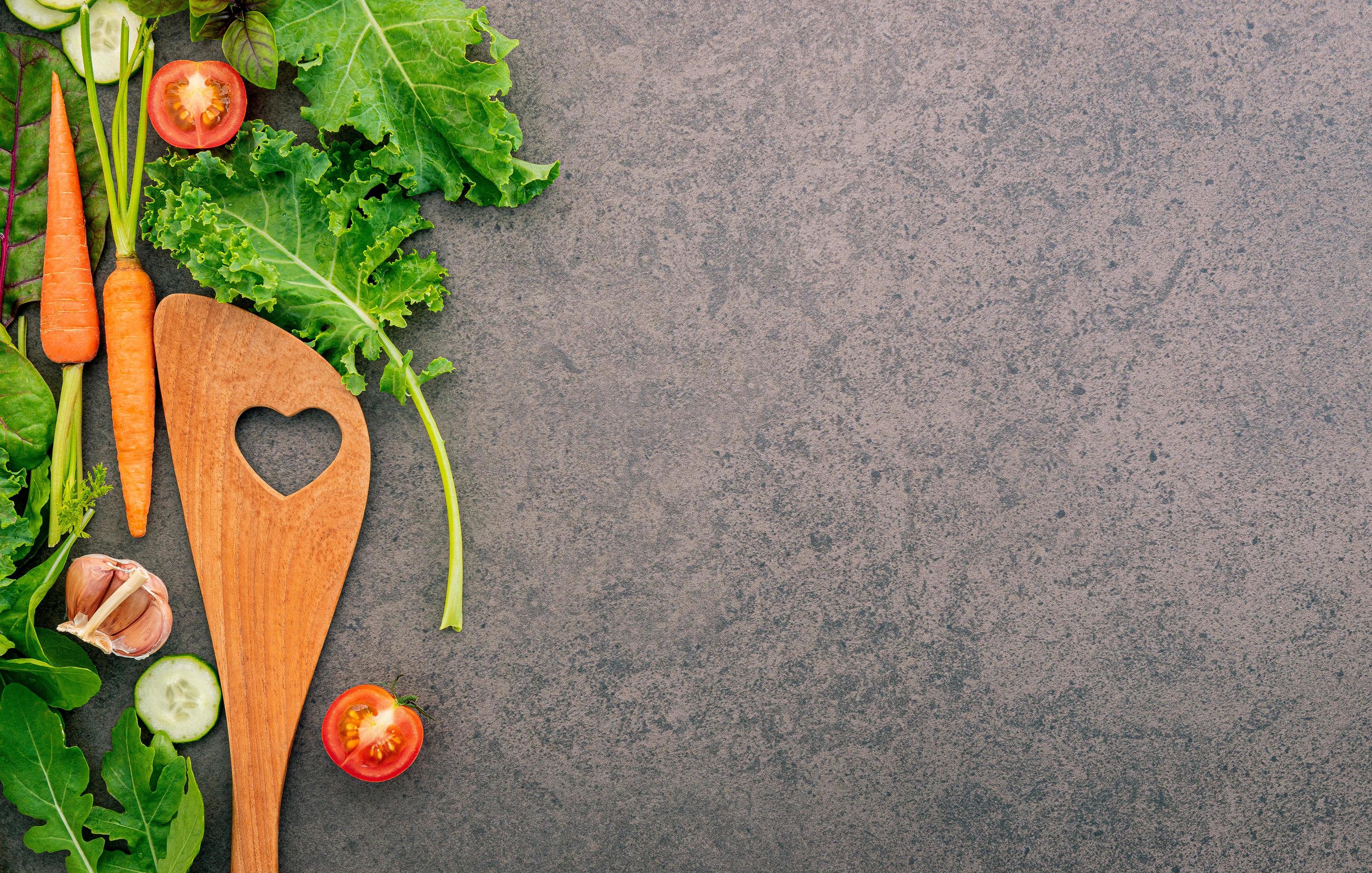 Wooden spatula and vegetables on a dark stone background. Healthy food and cooking concept. Stock Free