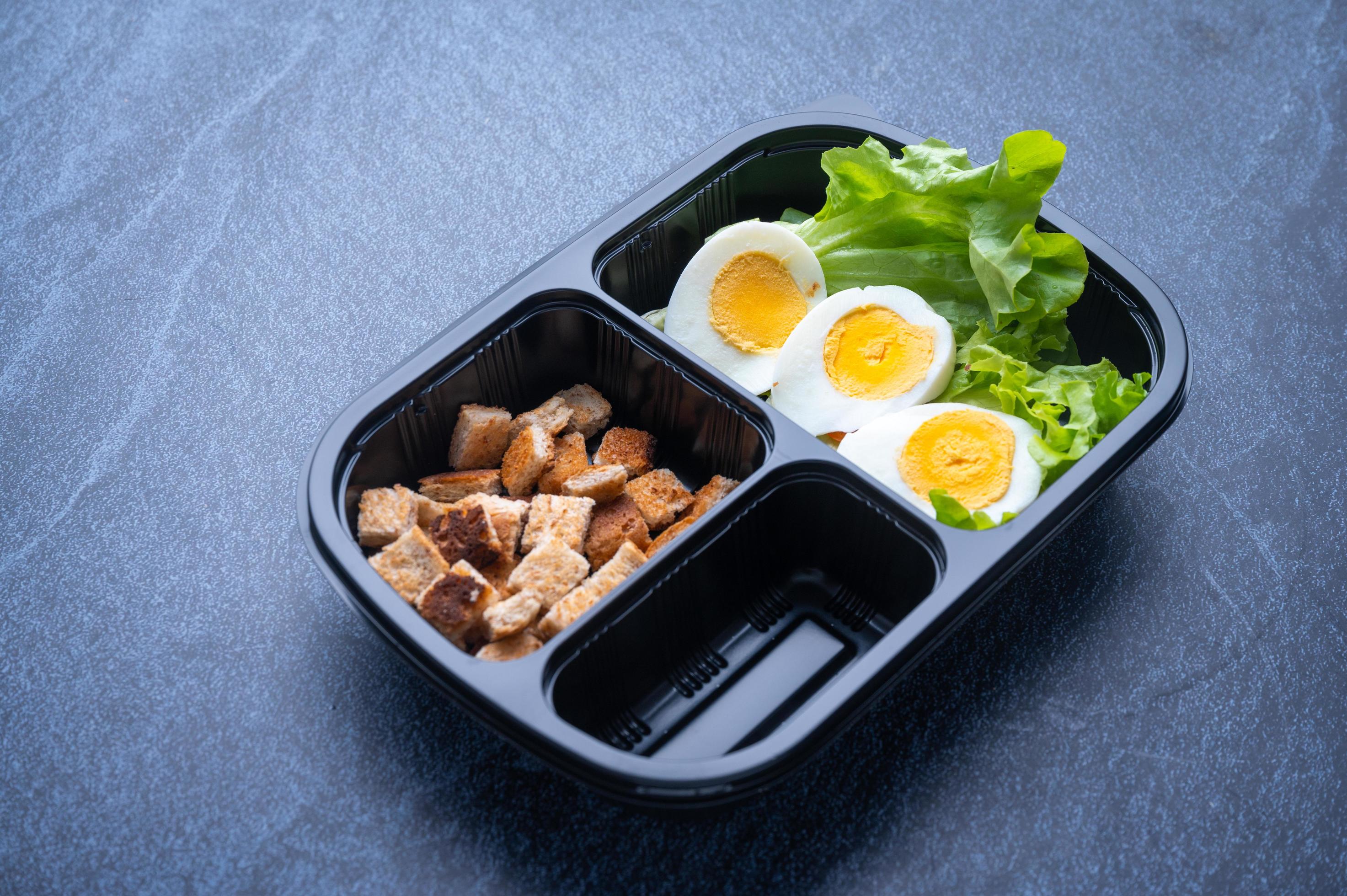 Sectioned plastic food container with croutons, lettuce, and sliced hard-boiled egg Stock Free