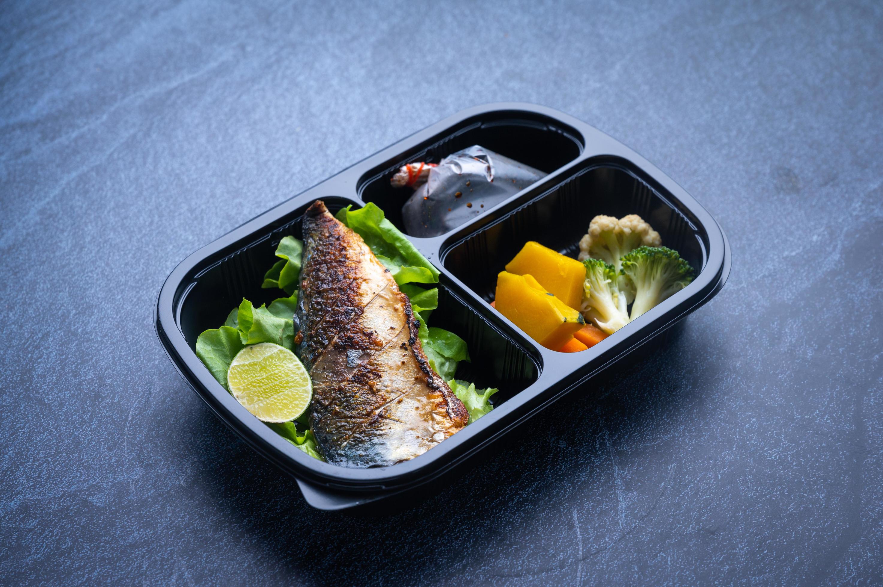 Sectioned plastic food container with salad, grilled fish, and vegetables Stock Free